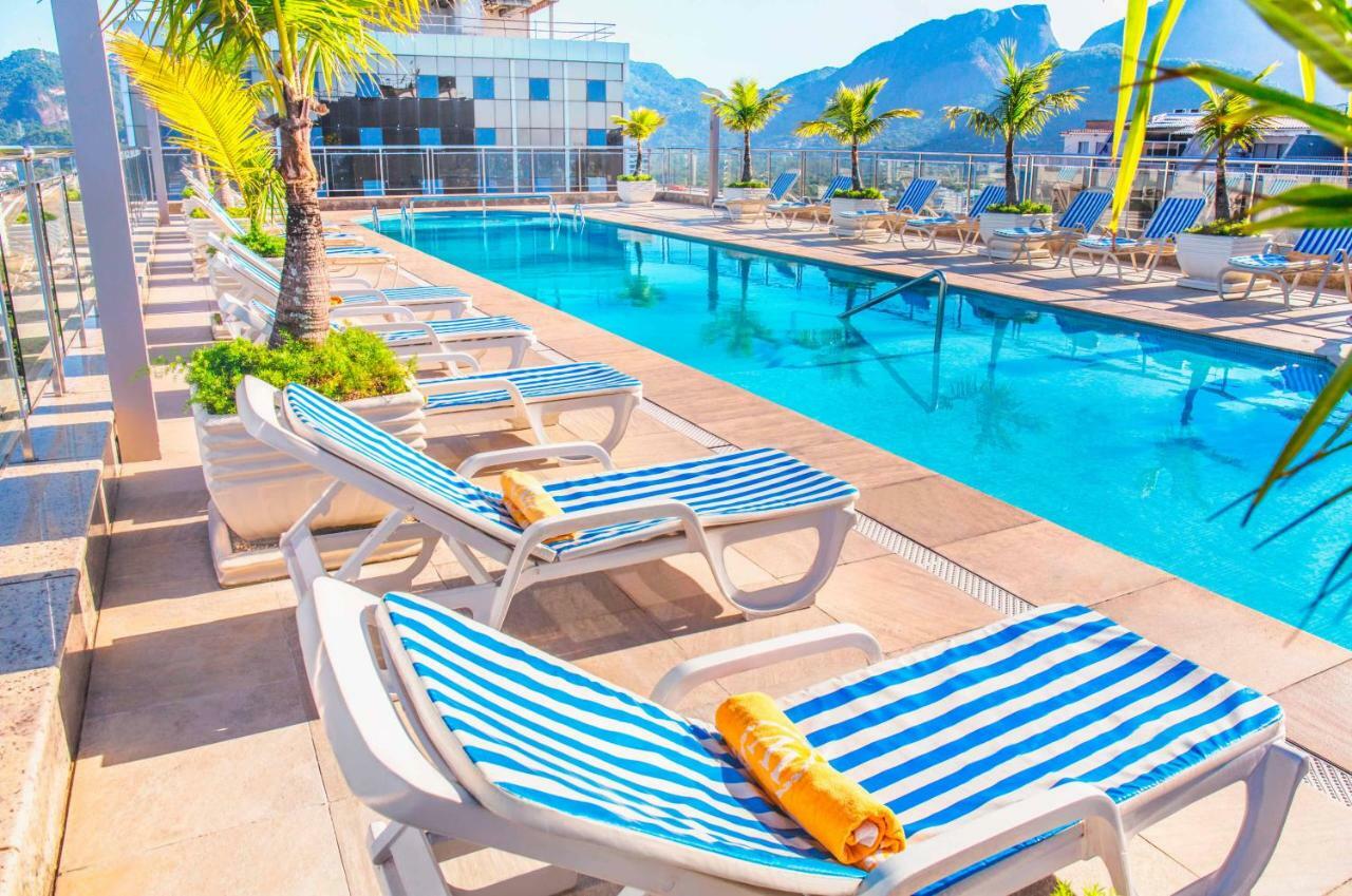 温莎芭拉酒店 里约热内卢 外观 照片 The photo shows a vibrant outdoor swimming pool area. There are several lounge chairs with blue and white striped cushions arranged around the pool. Some of the chairs have towels placed on them. In the background, the pool is clear and reflects the 